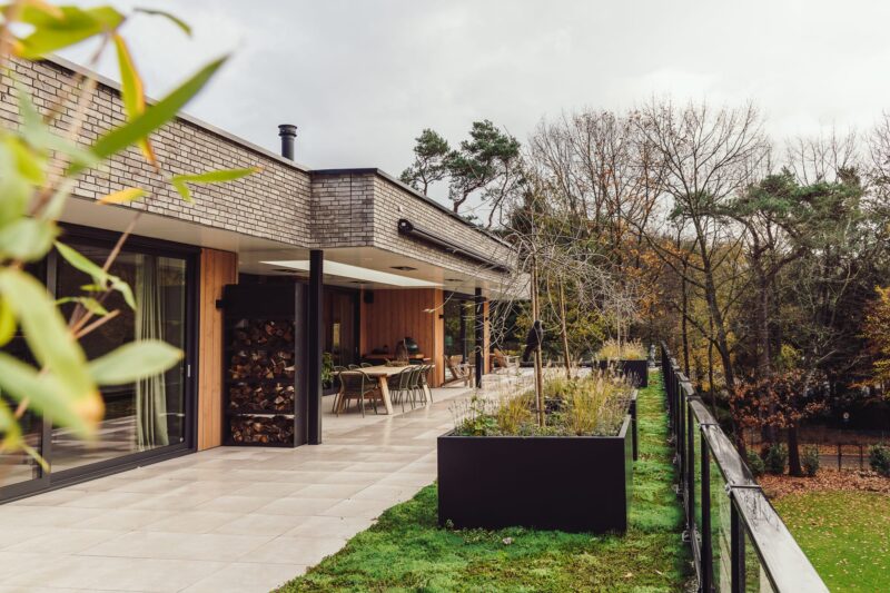 Zijaanzicht van appartementenvilla met bosrijke omgeving & tuinontwerp met overkapping in Den Dolder
